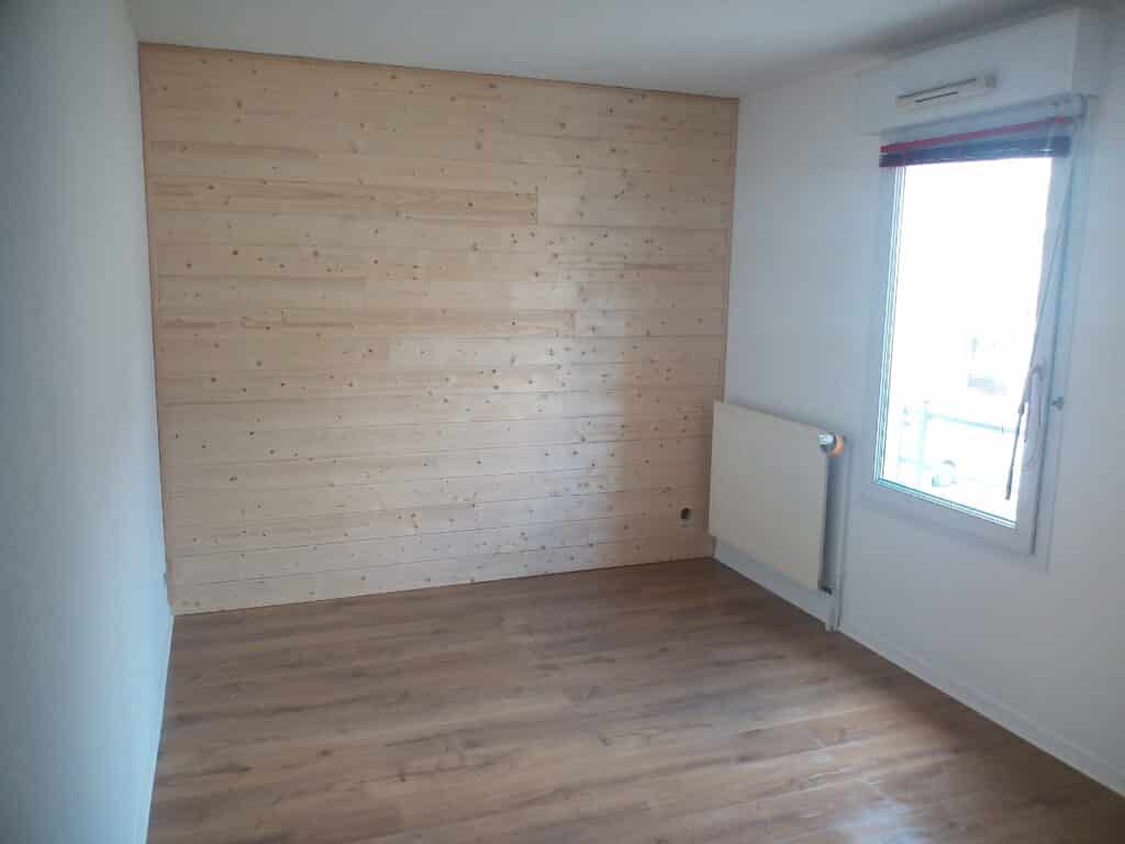 Chambre vide, mur d'accent en lambris de pin naturel. Plancher stratifié moderne, murs blancs et fenêtre latérale avec radiateur.